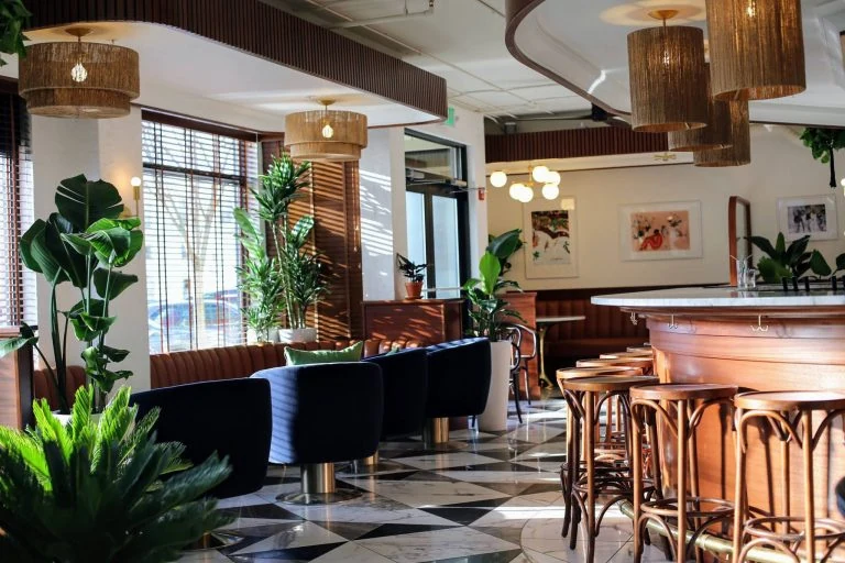Swim Club interior with tropical plants, warm wood and geometric floor tile.